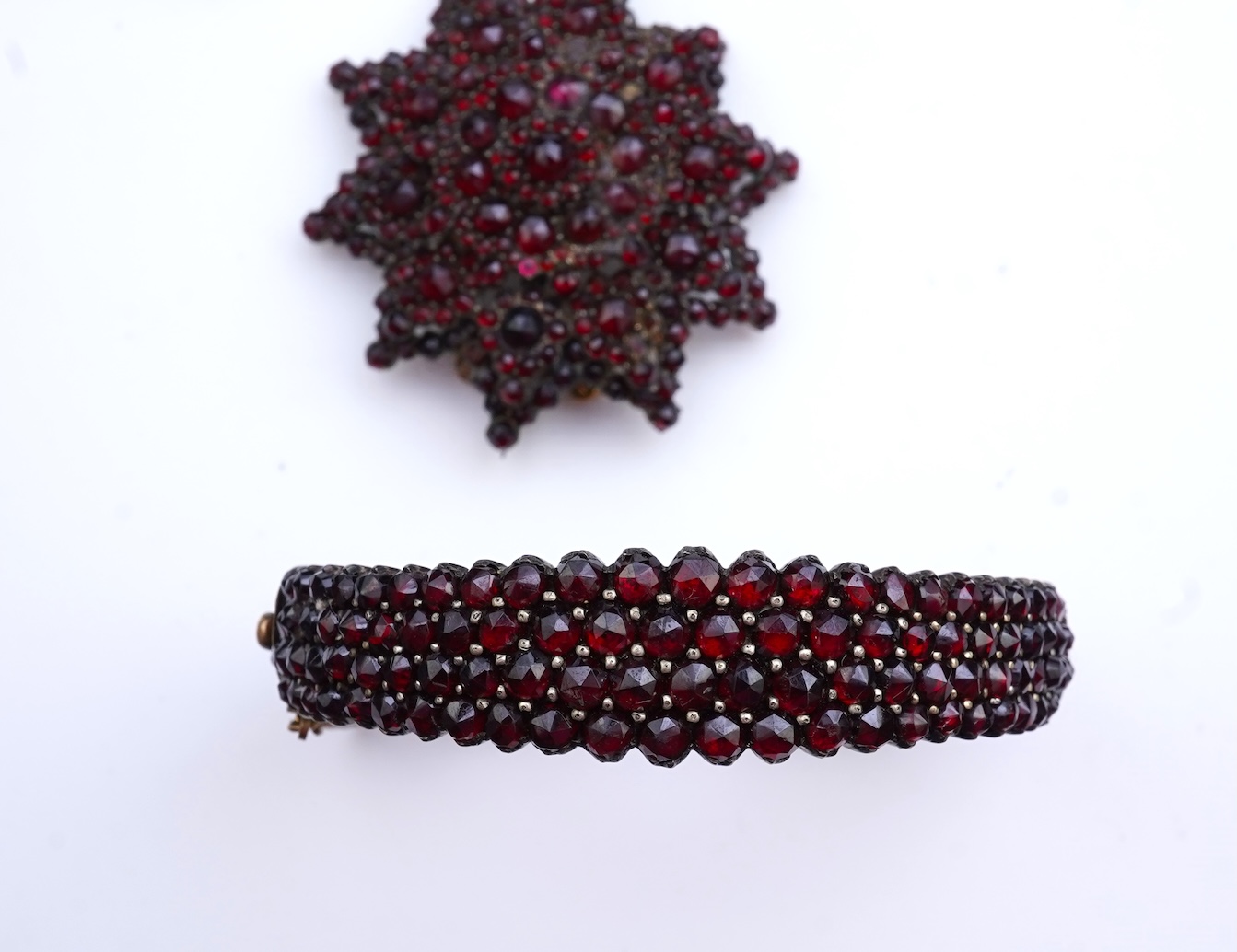 A suite of garnet and paste jewellery, comprising: a brooch, 5cm diameter; a bangle, inner circumference 16cm; two rings, sizes I and M; a pair of earrings, and a single earring, each set with rose-cut garnets; and a pai